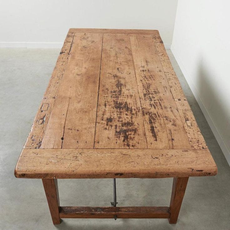 an old wooden table sitting on top of a cement floor next to a white wall