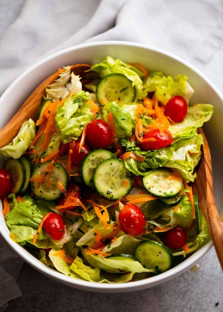 a salad with cucumbers, tomatoes and lettuce in a white bowl