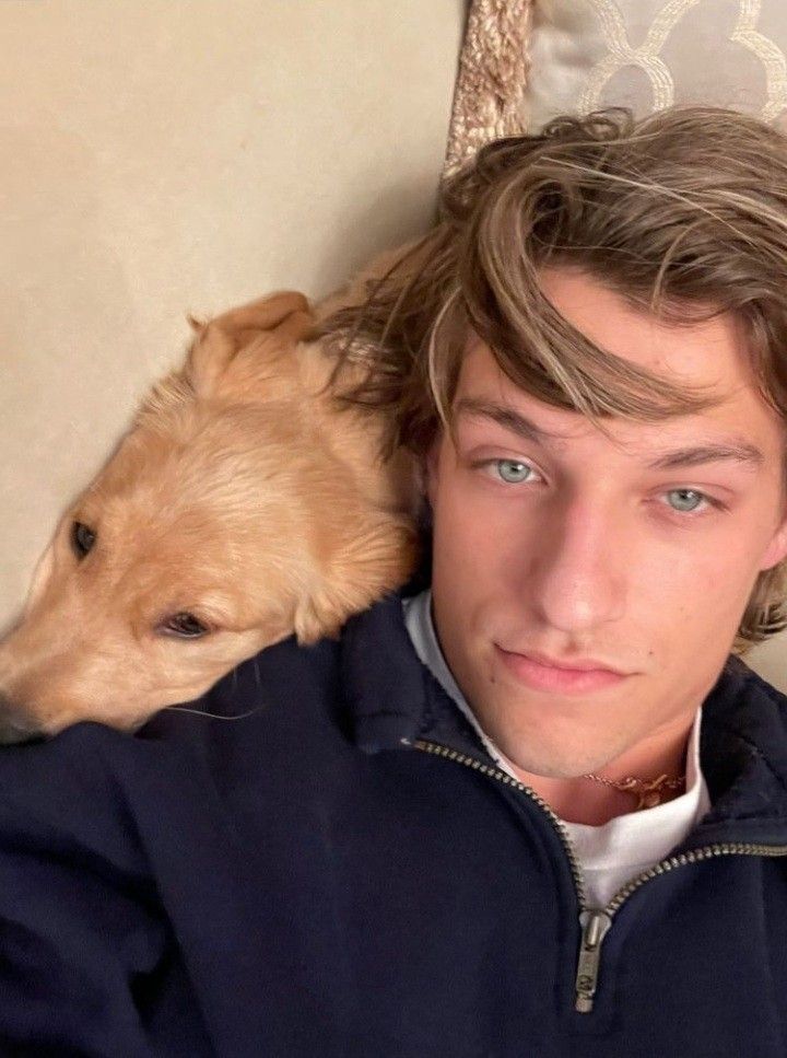 a young man laying on top of a couch next to a brown and white dog