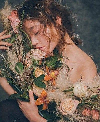 a woman with flowers and feathers on her chest holding something in her hand while looking down