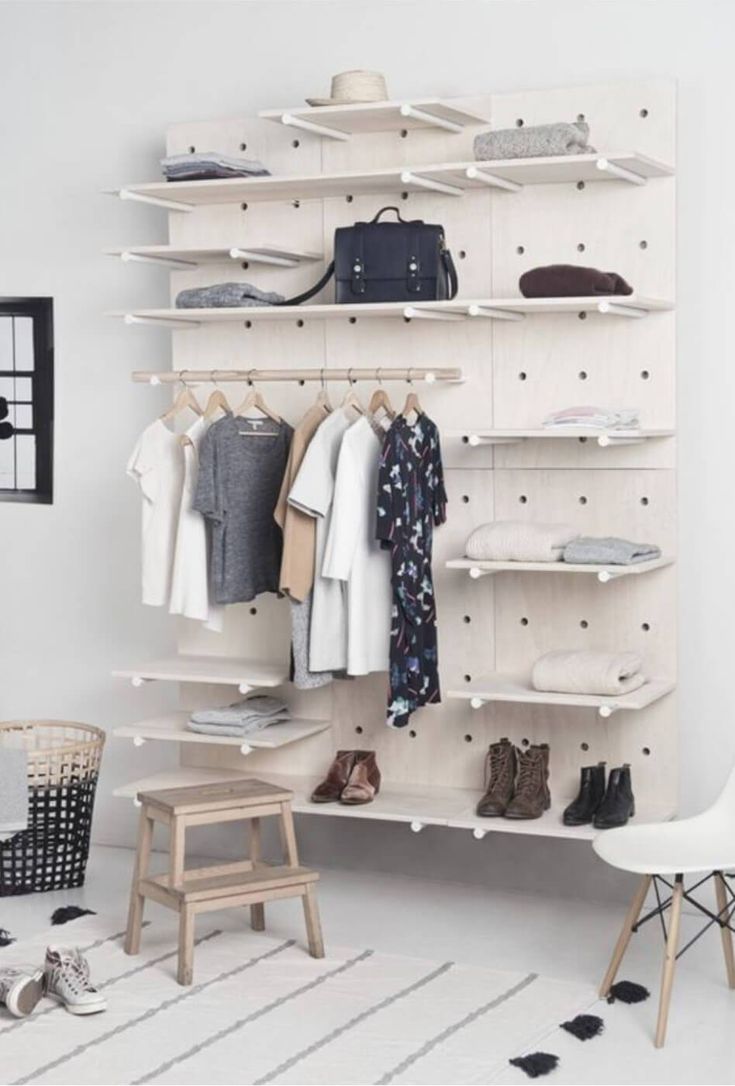 a white closet with clothes and shoes hanging on the wall next to a wooden stool