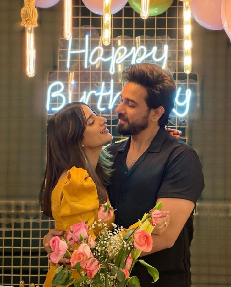 a man and woman standing next to each other in front of a birthday sign with balloons