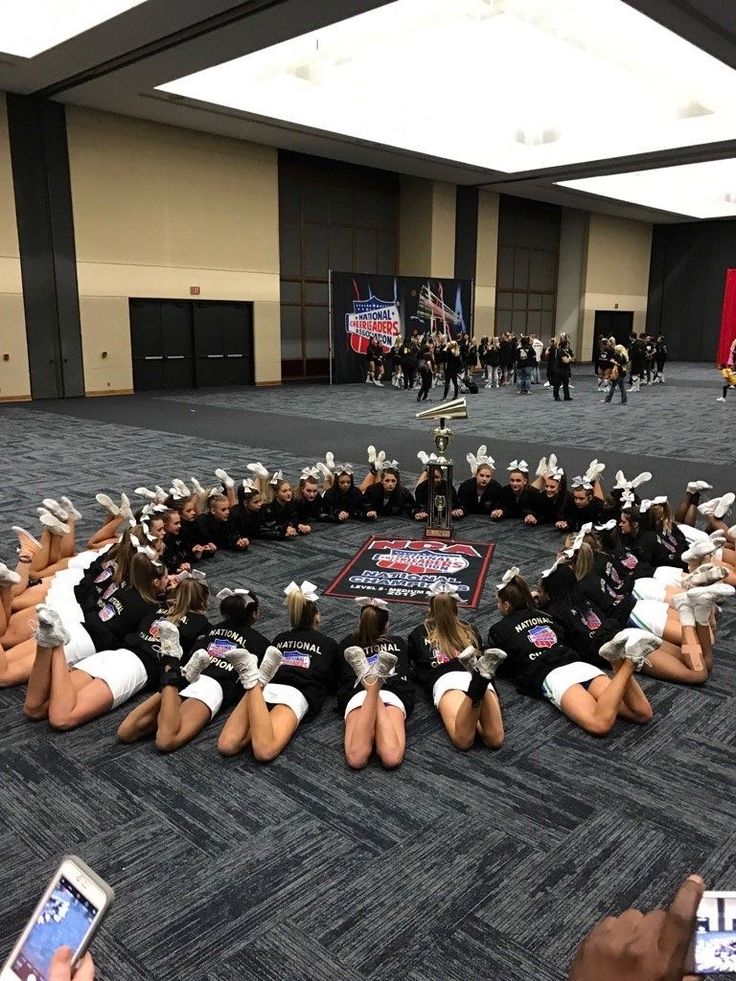 a group of cheerleaders sitting in a circle on the floor with their cell phones