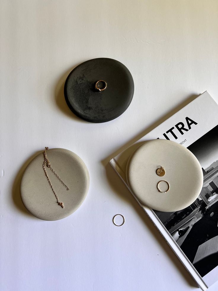 two white plates sitting on top of a table next to a magazine and ring dish