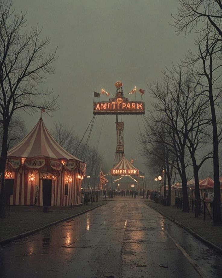 the entrance to an amusement park is lit up with lights and umbrellas on a rainy day