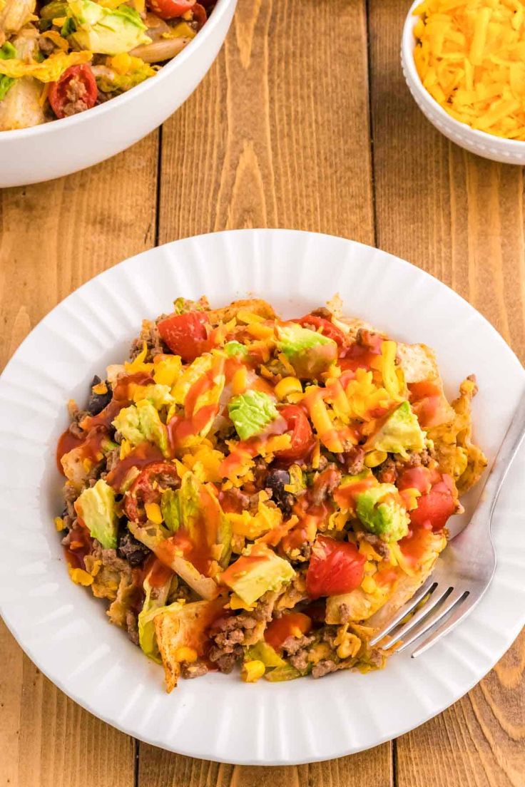 a white plate topped with taco salad next to a bowl of shredded cheese