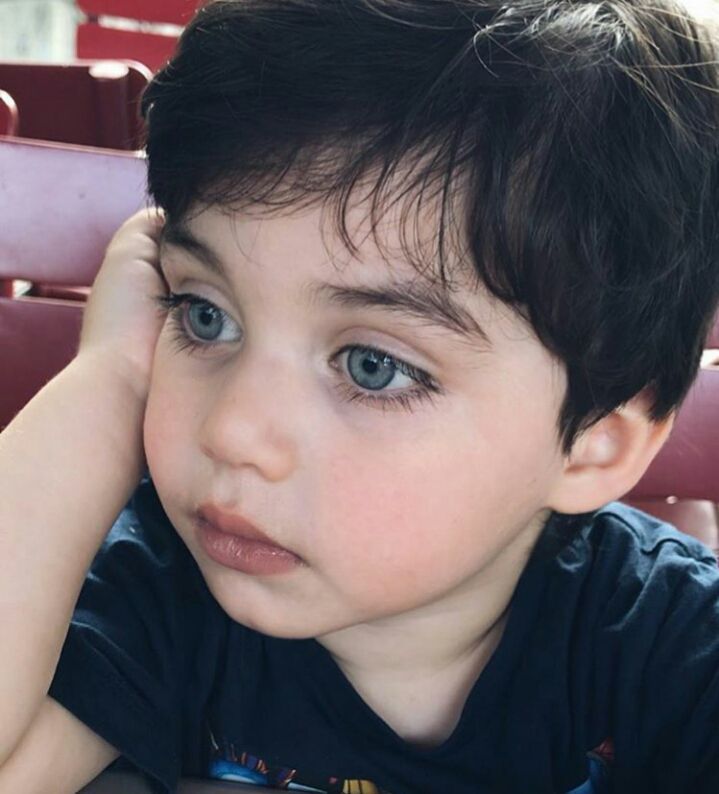 a young boy sitting at a table with his hand on his head and looking off to the side