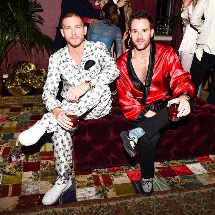 two men sitting on a couch in front of a group of people at a party