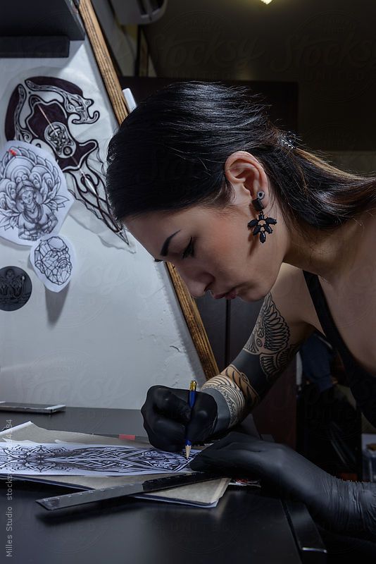 a woman in black gloves writing on a piece of paper by a wall with tattoos