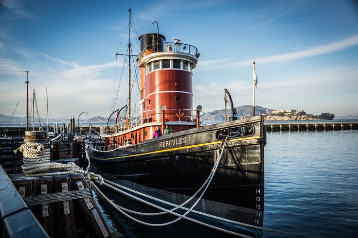 a large red and black boat docked at a pier with other boats in the background