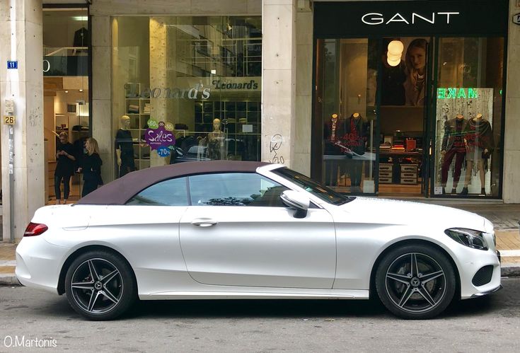 a white convertible car parked in front of a storefront with people walking by it