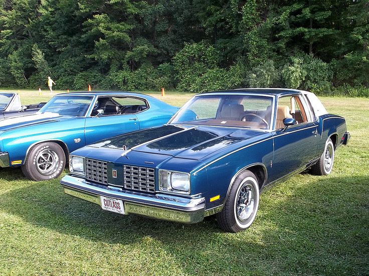 two old cars parked next to each other in a grassy field with trees in the background