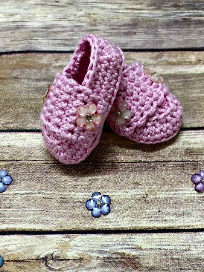 two pink crocheted baby shoes sitting on top of a wooden floor next to flowers