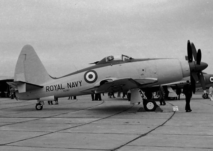 an old royal navy plane is parked on the tarmac with people around it and several other planes in the background