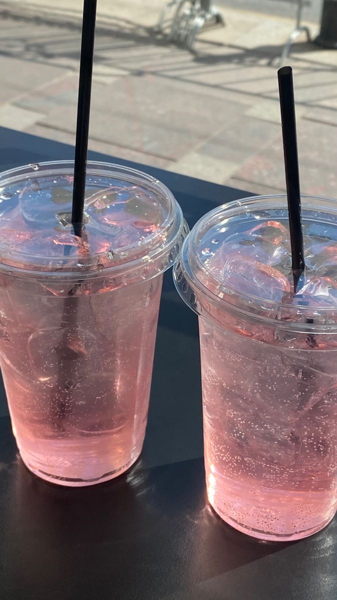 two plastic cups filled with pink liquid sitting on top of a table next to each other