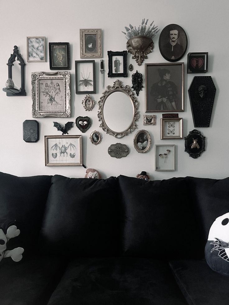 a black couch sitting in front of a white wall covered with pictures and framed objects