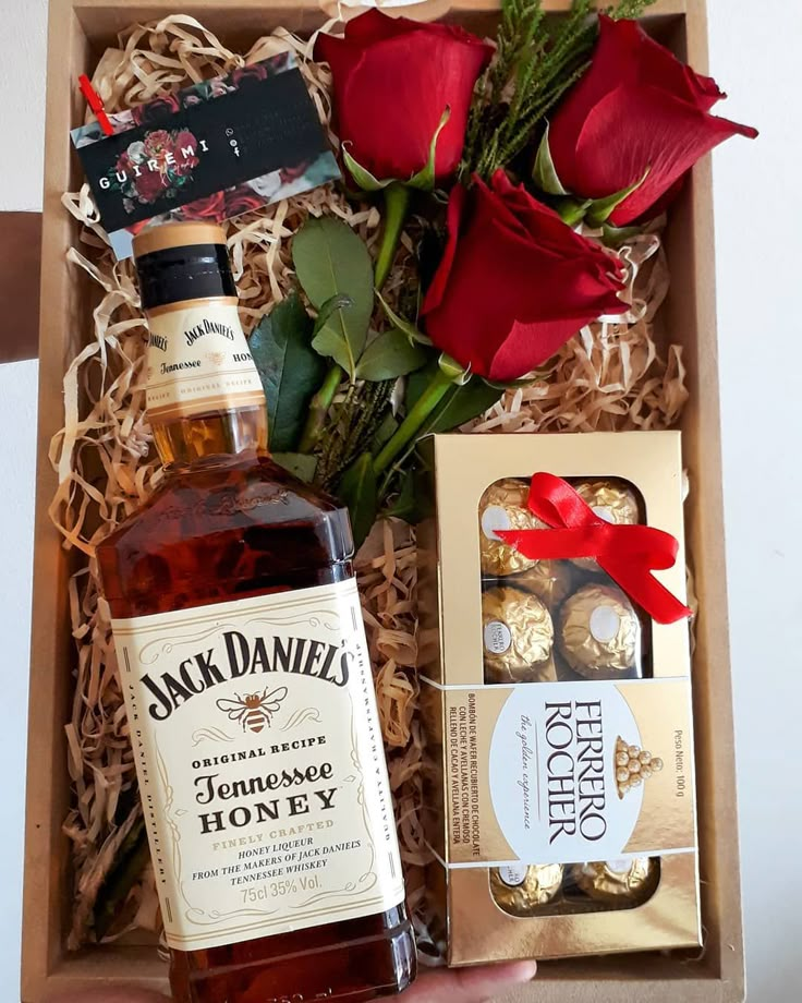 a bottle of whiskey and some chocolates in a gift box with red roses on the table