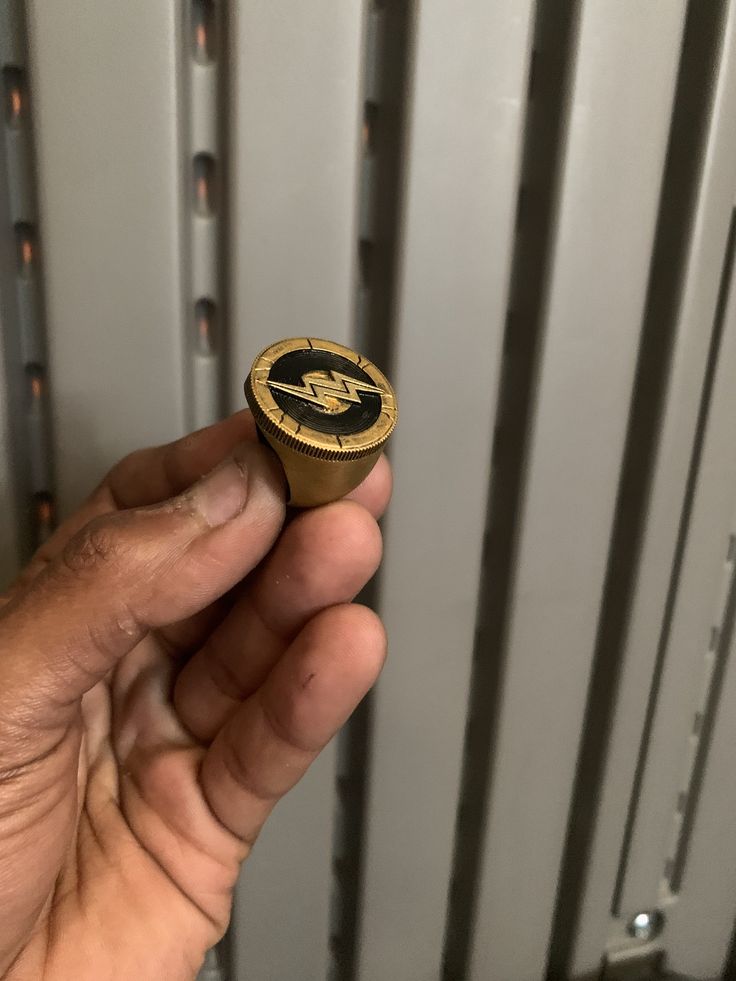 a hand holding a gold and black ring in front of a radiator with the letter c on it