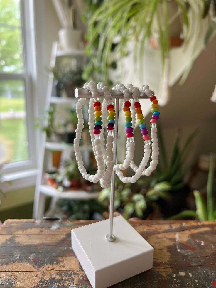 a white stand with beads on it in front of a potted plant