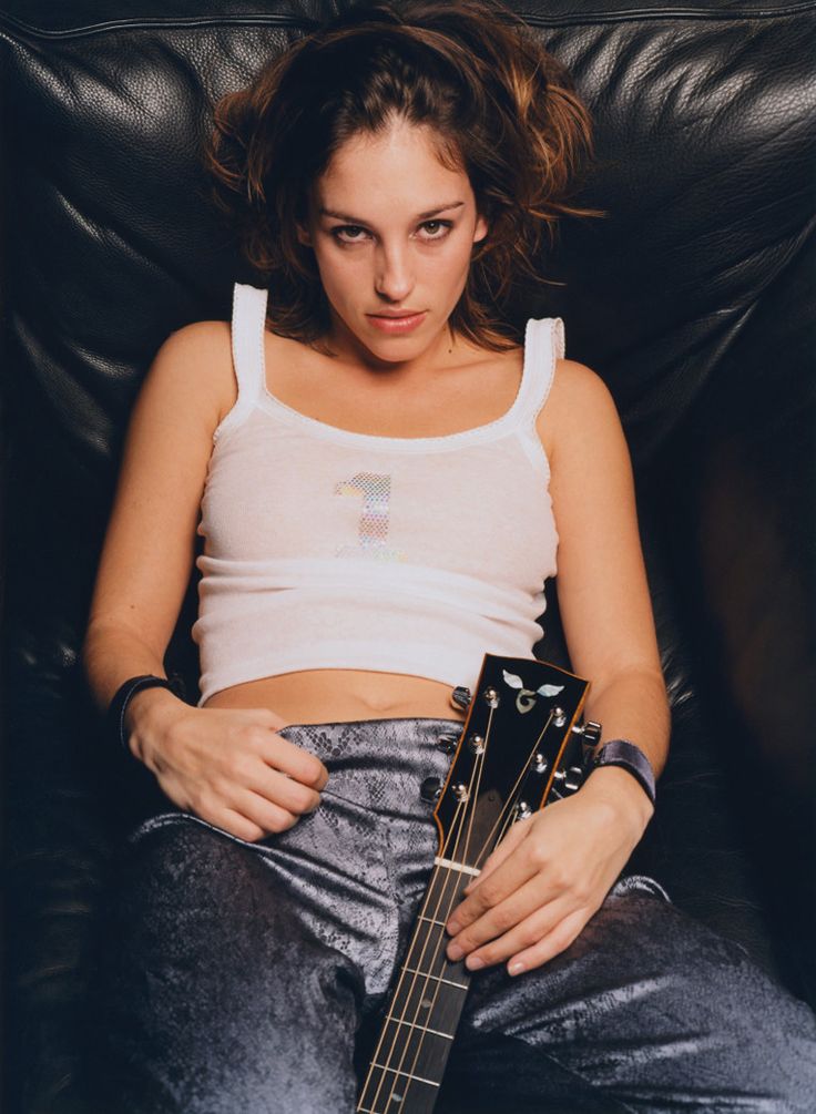 a woman sitting in a chair holding a guitar and looking at the camera with her eyes closed