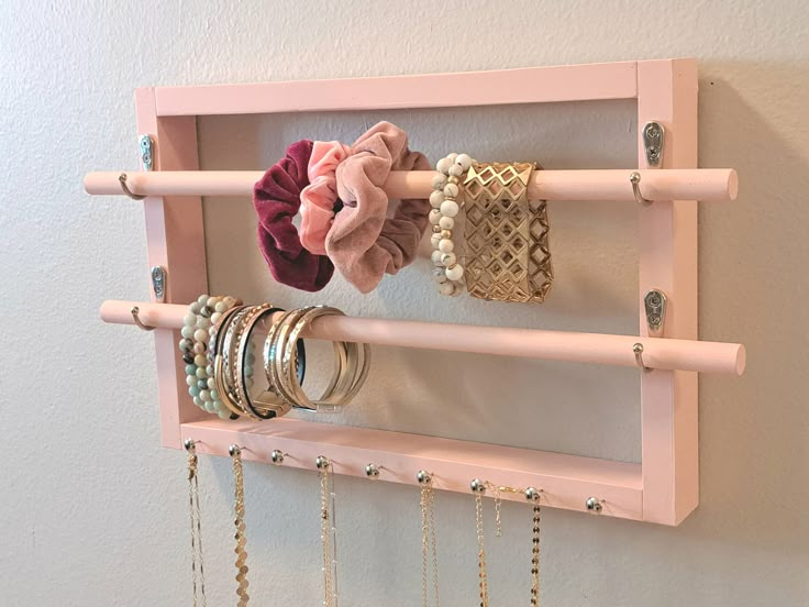 a pink rack with rings and bracelets hanging on it's sides next to a wall