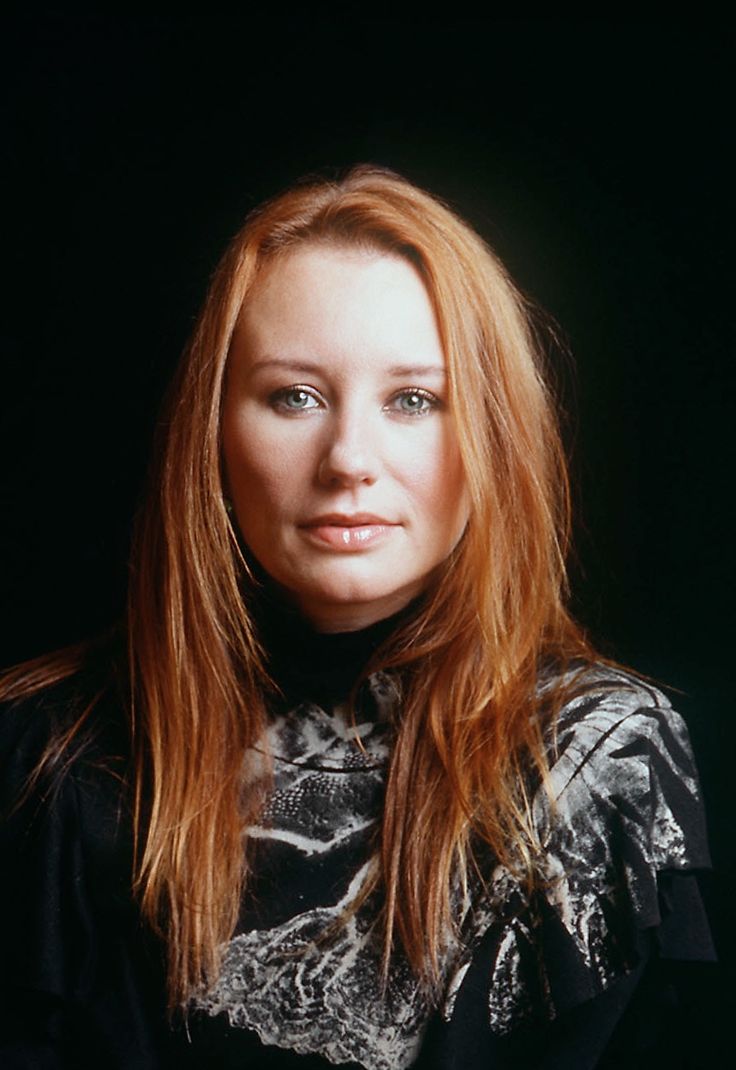 a woman with long red hair and blue eyes posing for a photo in front of a black background