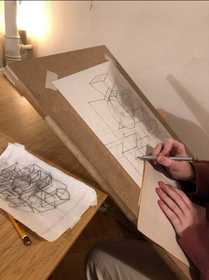 a person sitting at a table with some drawings on paper and pencils in front of them