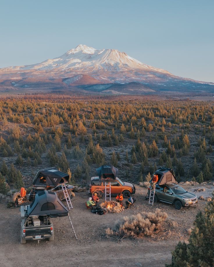 three cars parked in the middle of a field with a mountain in the back ground