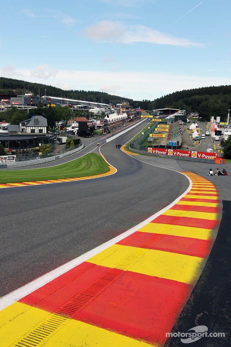 a race track with red and yellow painted lines on it, surrounded by small town in the background