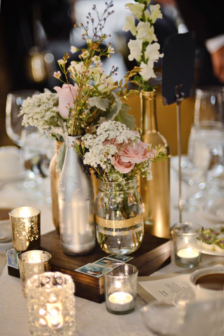 the table is set with silver and gold vases, candles, and flower centerpieces