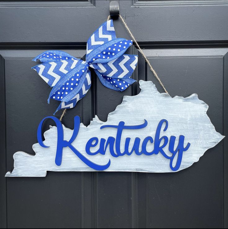 a kentucky state shaped sign hanging on a door with a blue bow and polka dot ribbon