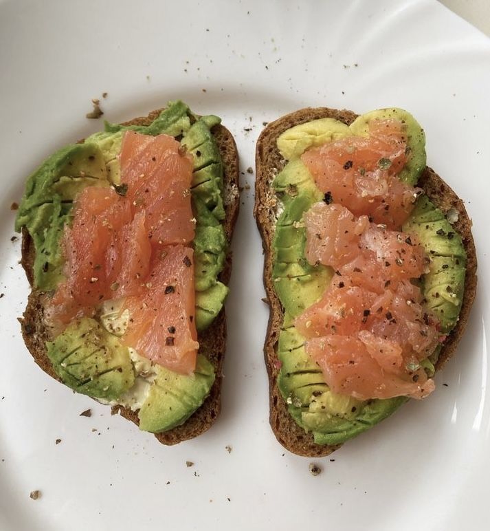 two pieces of bread with salmon and avocado on them sitting on a plate