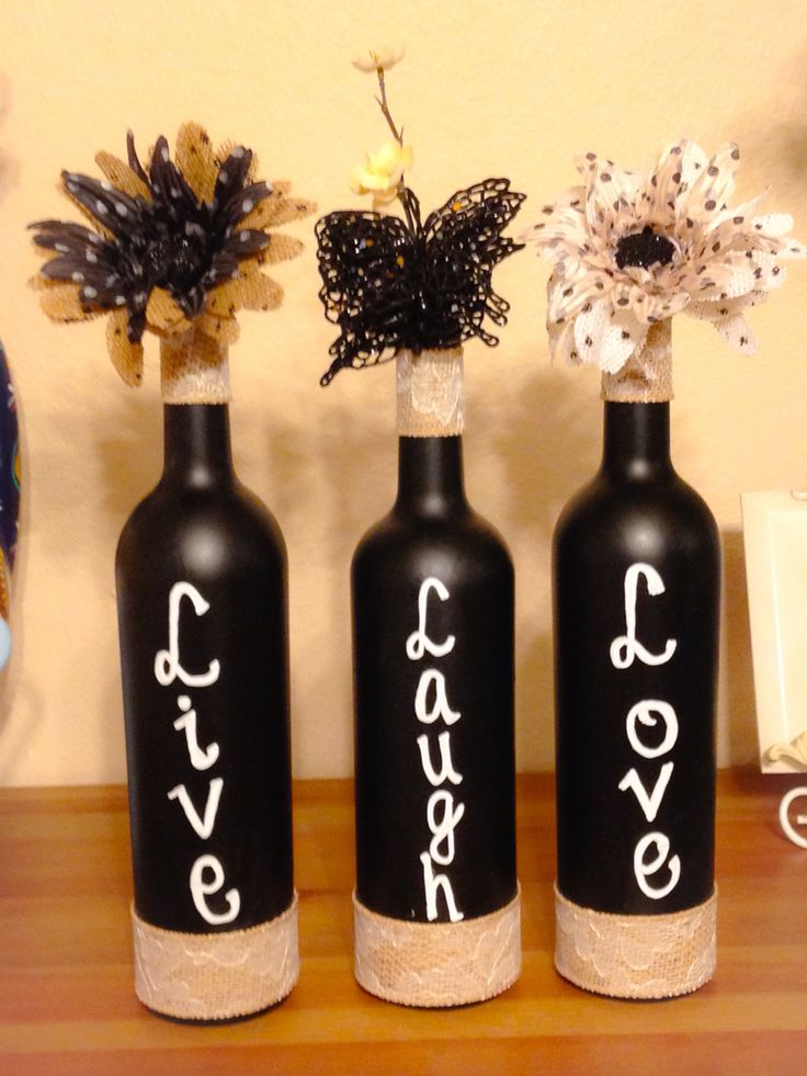 three black bottles with white writing on them are sitting on a wooden table and one has a flower in it