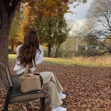 a woman is sitting on a bench in the park with autumn leaves all around her