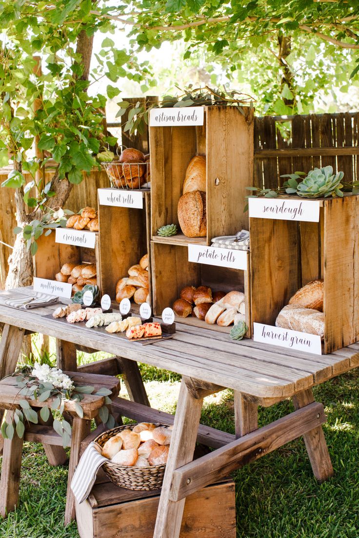 a wooden table topped with lots of different types of bread on display next to a tree