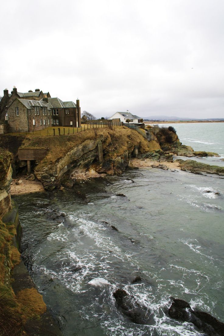 an old castle sitting on top of a cliff next to the ocean with waves coming in