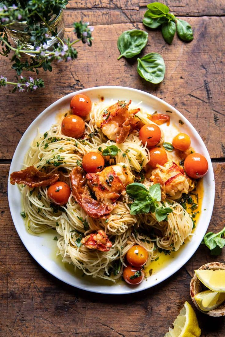 a plate of pasta with shrimp, tomatoes and basil on the side next to sliced lemon wedges