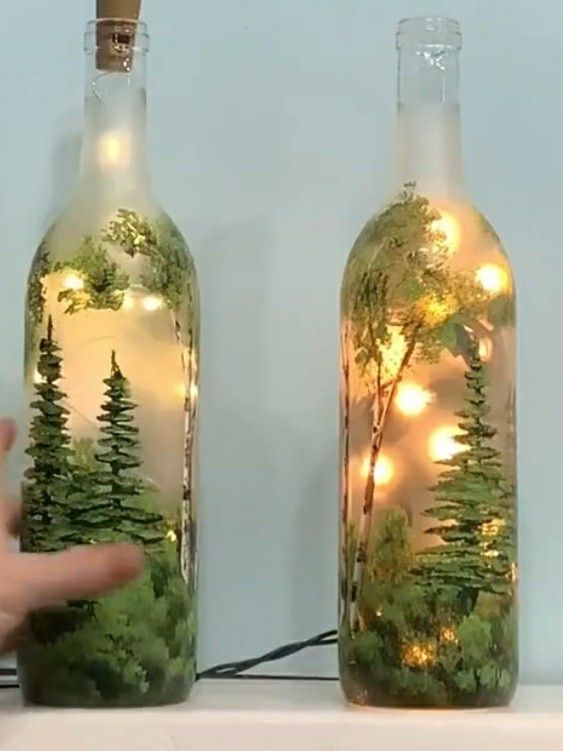 two bottles with trees in them and lights inside