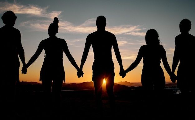 four people holding hands with the sun setting behind them