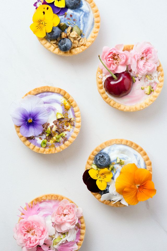 three pies with flowers and fruit on them sitting next to each other in front of a white background