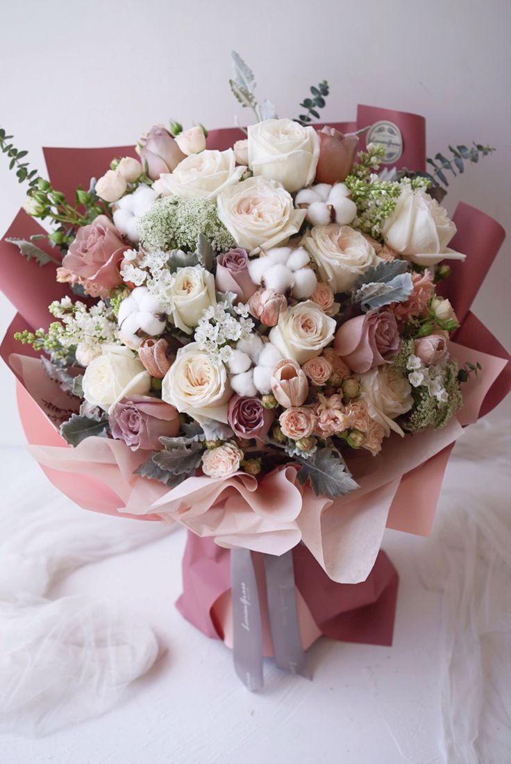 a bouquet of flowers sitting on top of a white table next to a pink ribbon