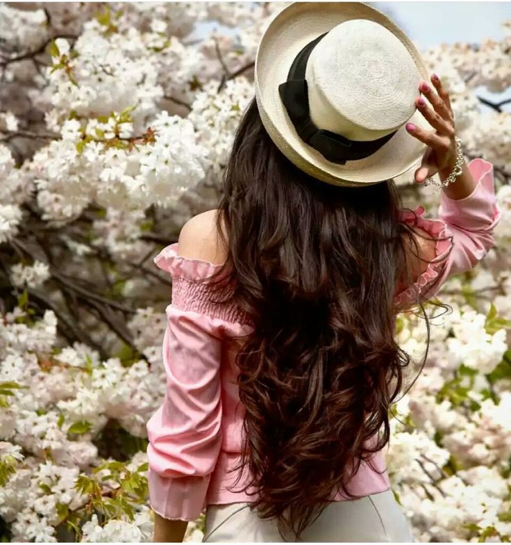 a woman with long hair wearing a hat in front of some flowers on the tree