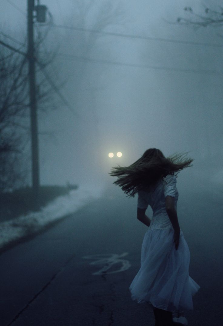 a woman is walking down the street with her hair blowing in the wind at night