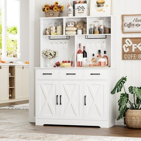 a white cabinet filled with lots of bottles and glasses next to a potted plant