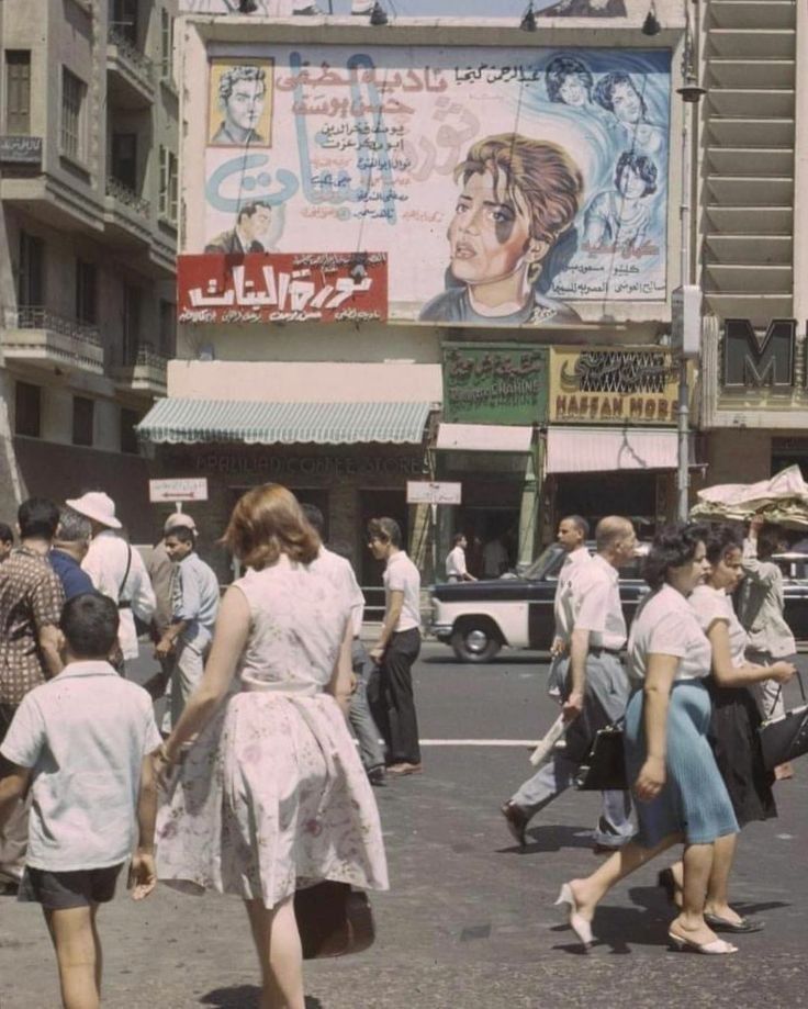 an old photo of people crossing the street in front of a movie advertisement on a building