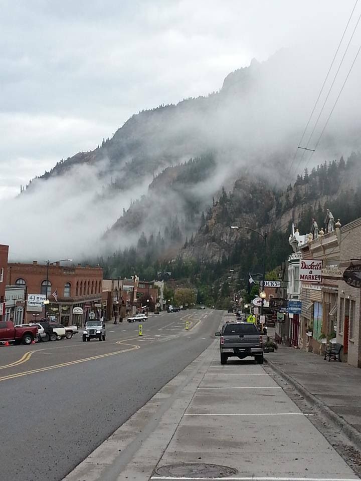 cars parked on the side of a road in front of a mountain covered with clouds