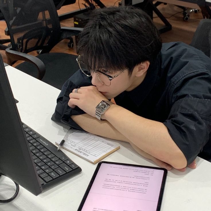 a young man sitting at a desk in front of a laptop computer with a pad on it