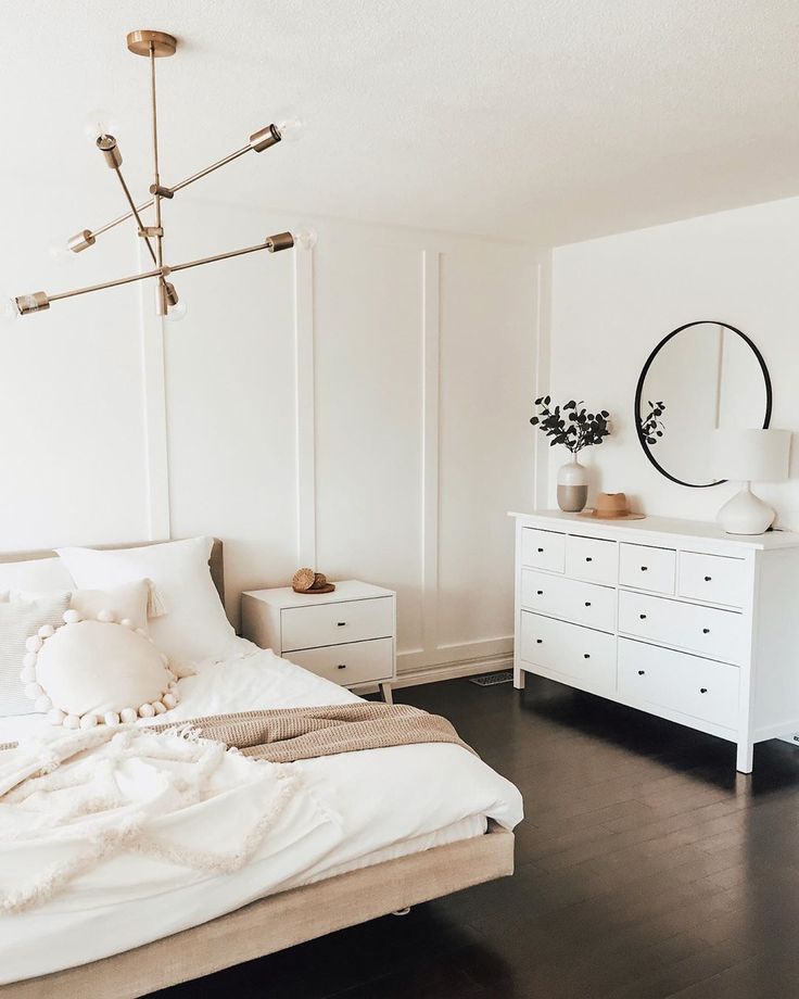 a bedroom with white walls and wooden floors has a bed, dresser, and mirror