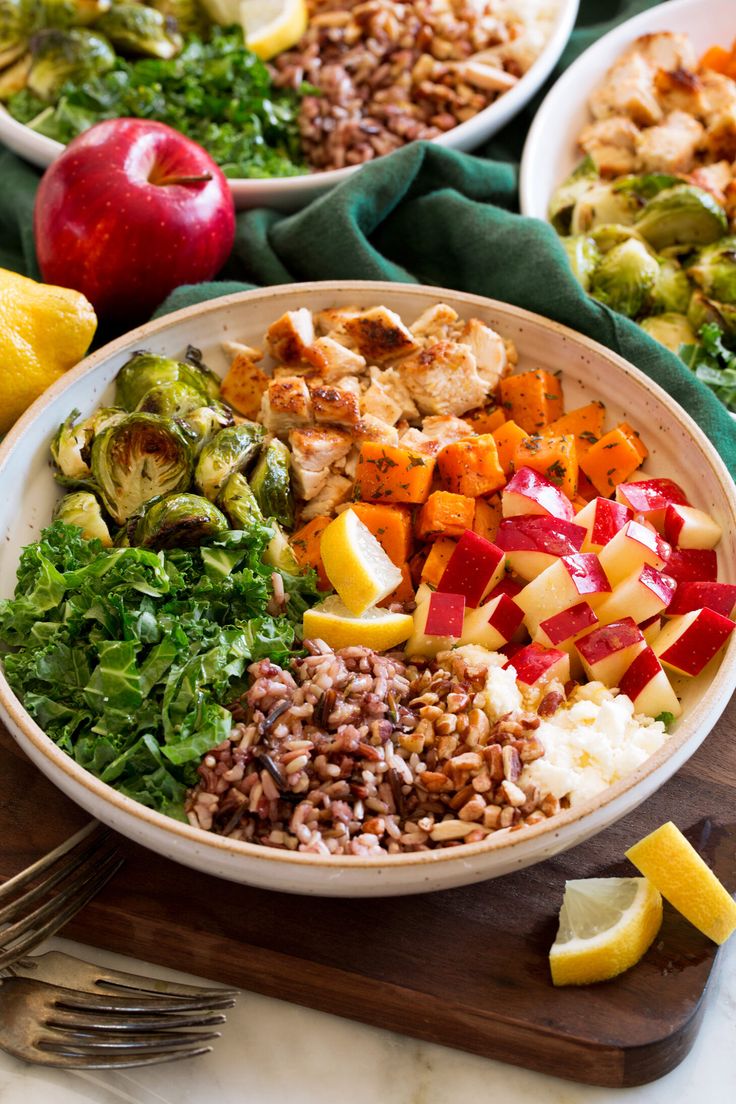 two bowls filled with different types of food on top of a wooden cutting board next to silverware