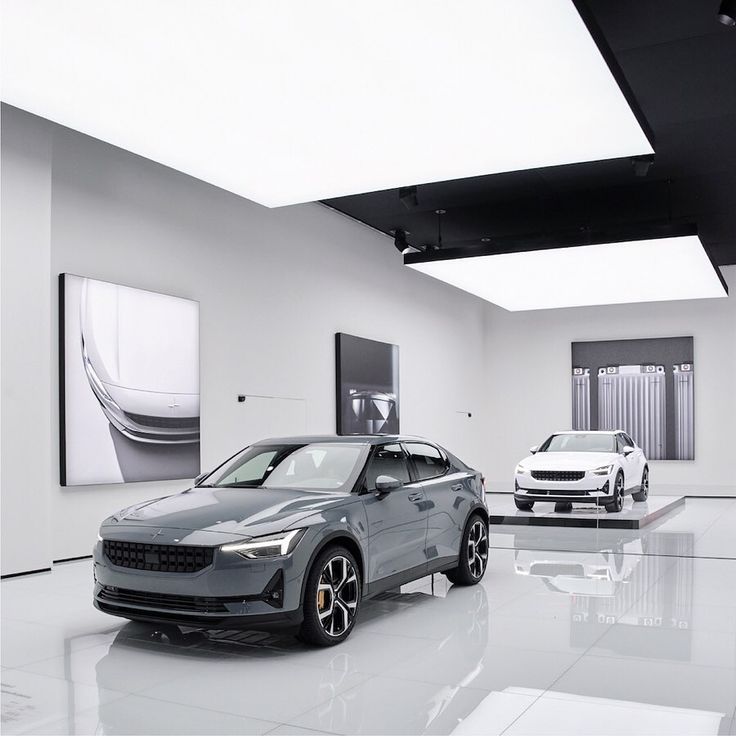 two cars are parked in a showroom with white walls and black ceiling tiles on the floor